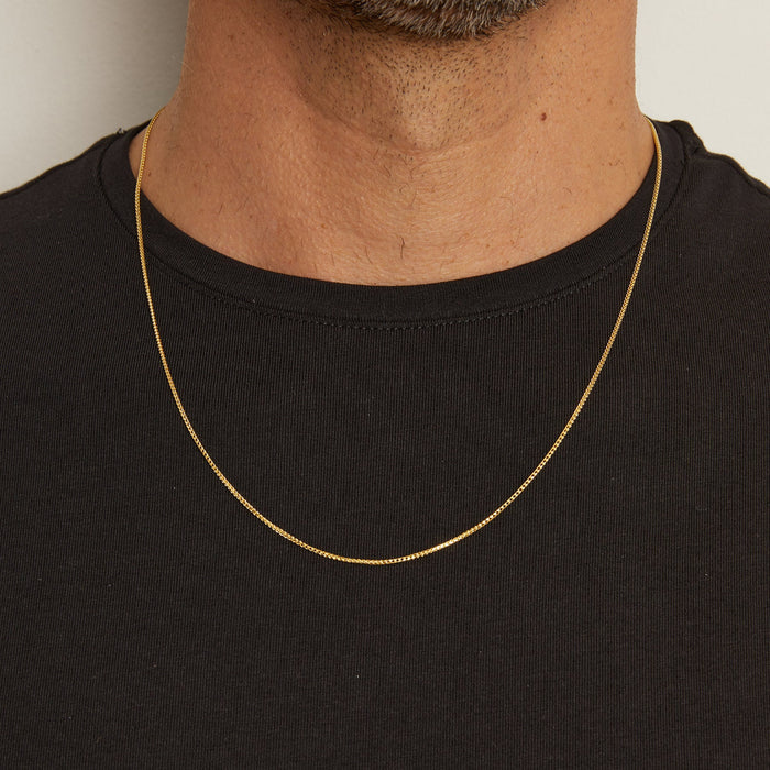 Model. Man wearing a gold chain necklace against a neutral background