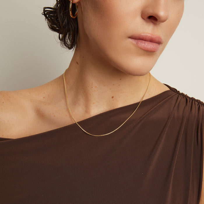 Model. Woman wearing a gold necklace with a plain background