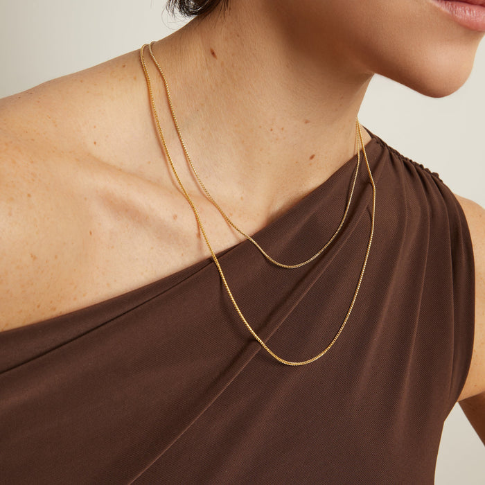 Model. Woman wearing a gold necklace with a plain background