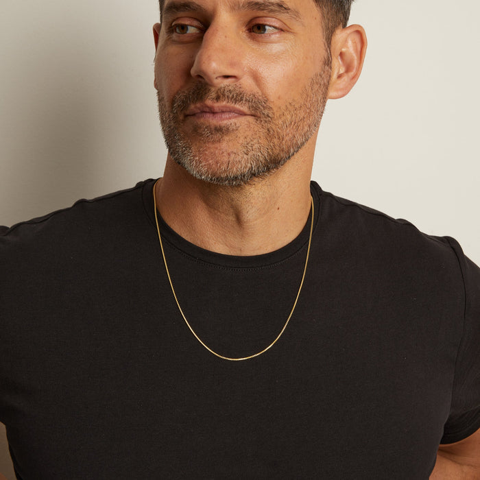 Man wearing a black t-shirt and gold necklace against a neutral background