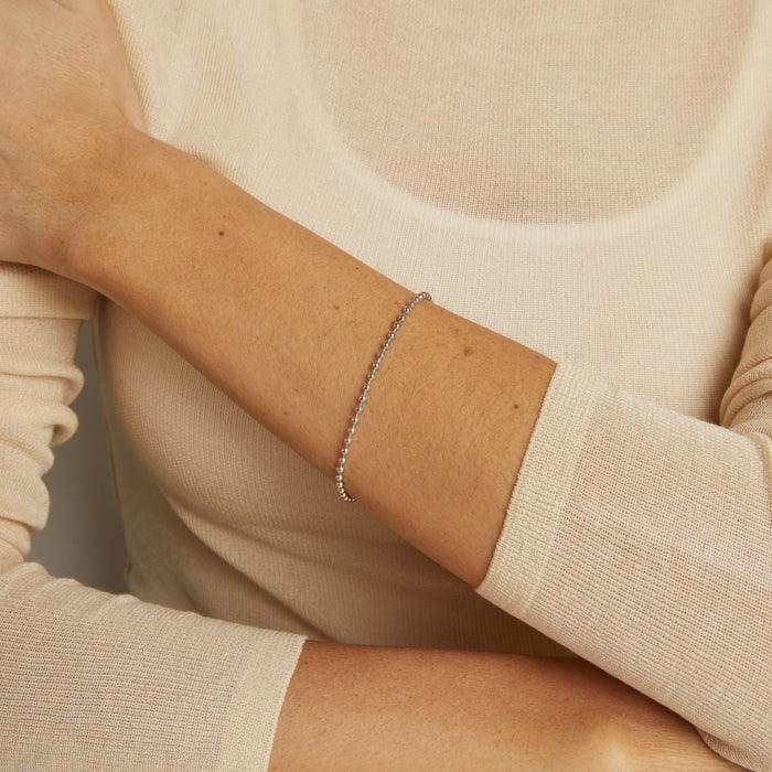 Close-up of a person wearing a silver bracelet on a neutral background