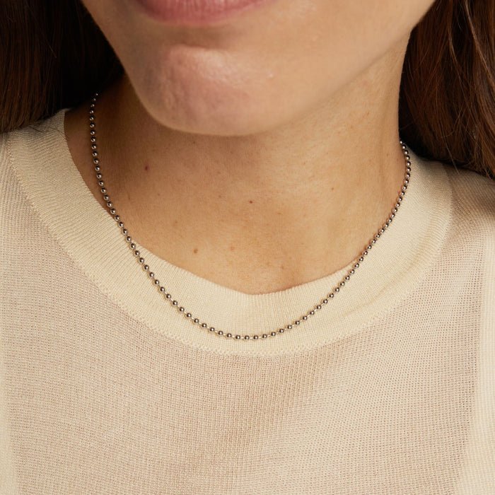 Model. Close-up of a person wearing a delicate silver necklace against a neutral background