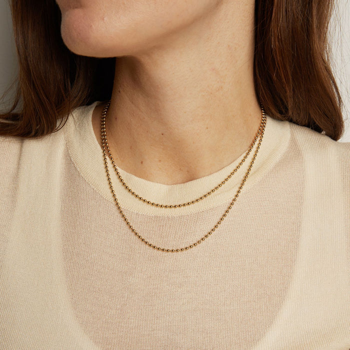 Model. Close-up of a person wearing a delicate gold necklace against a neutral background
