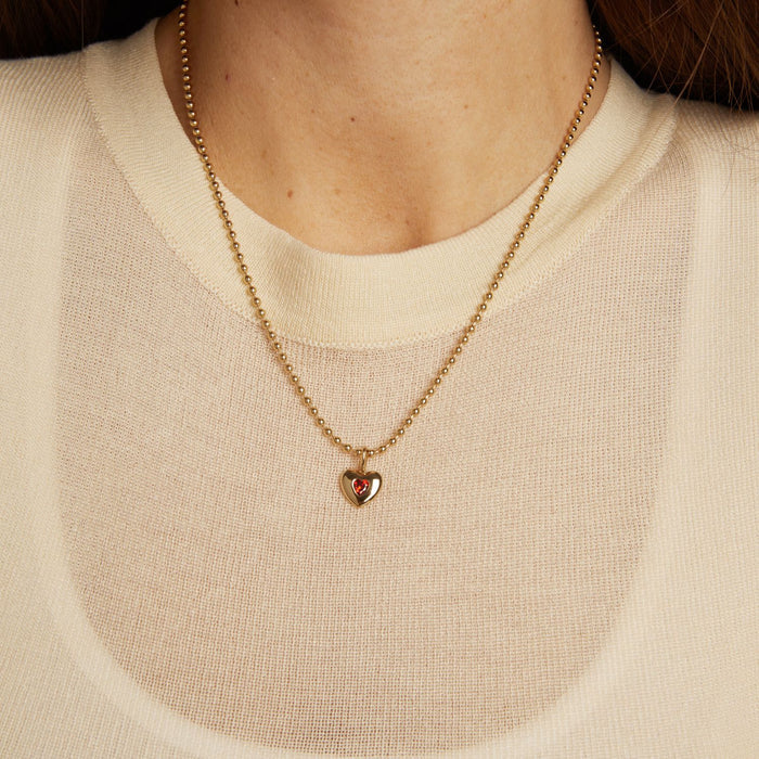 Model. Gold necklace with a heart pendant worn by a person in a beige sweater.