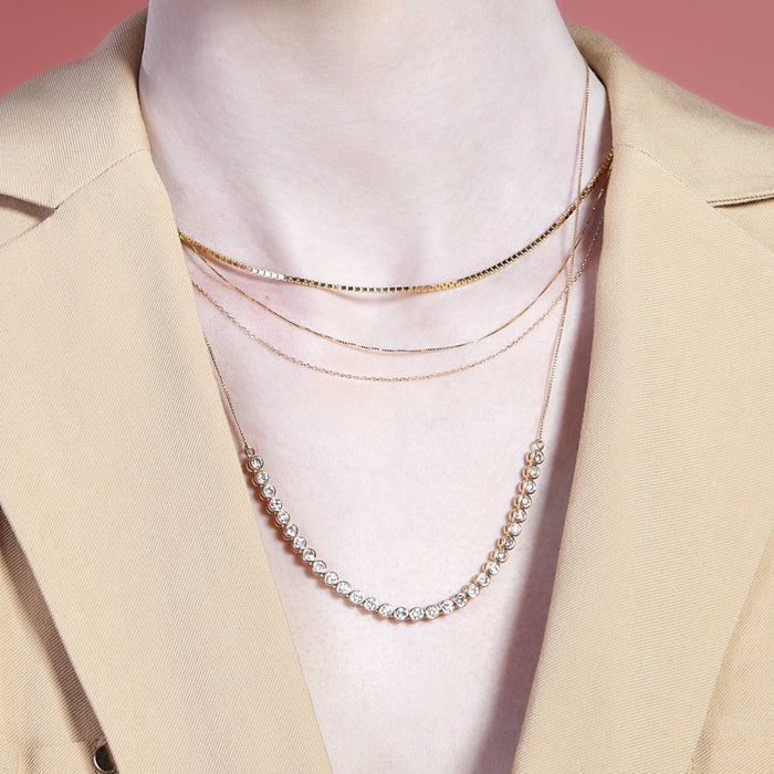 Lifestyle Model Close-up of a woman wearing a tan blazer and three layered gold necklaces.