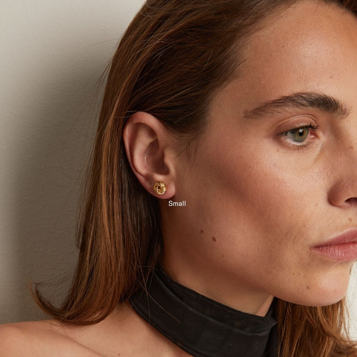 Model. Close-up of a woman wearing a gold earring with a neutral background
