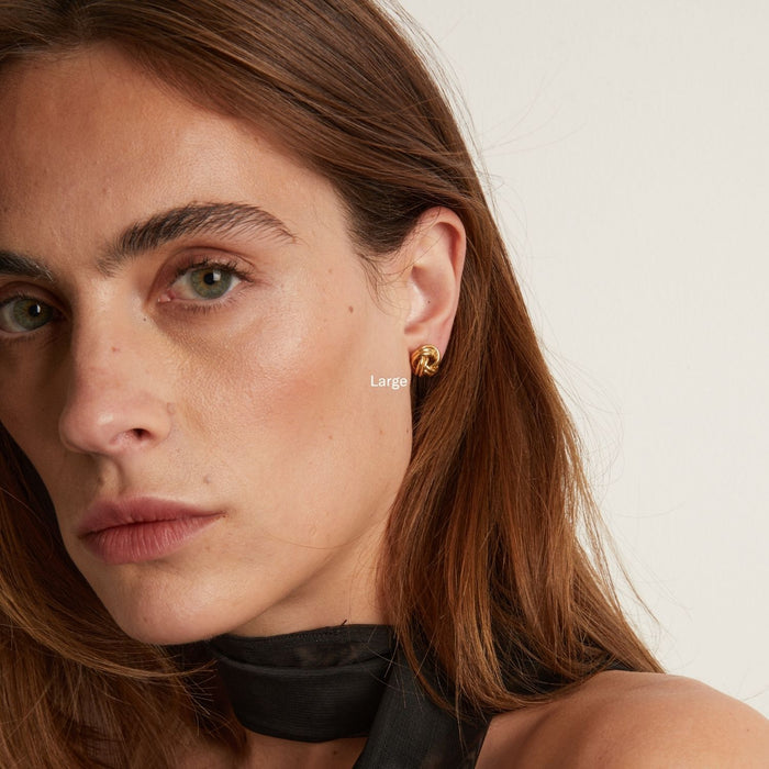 Model. Close-up of a person wearing gold earrings with a neutral background
