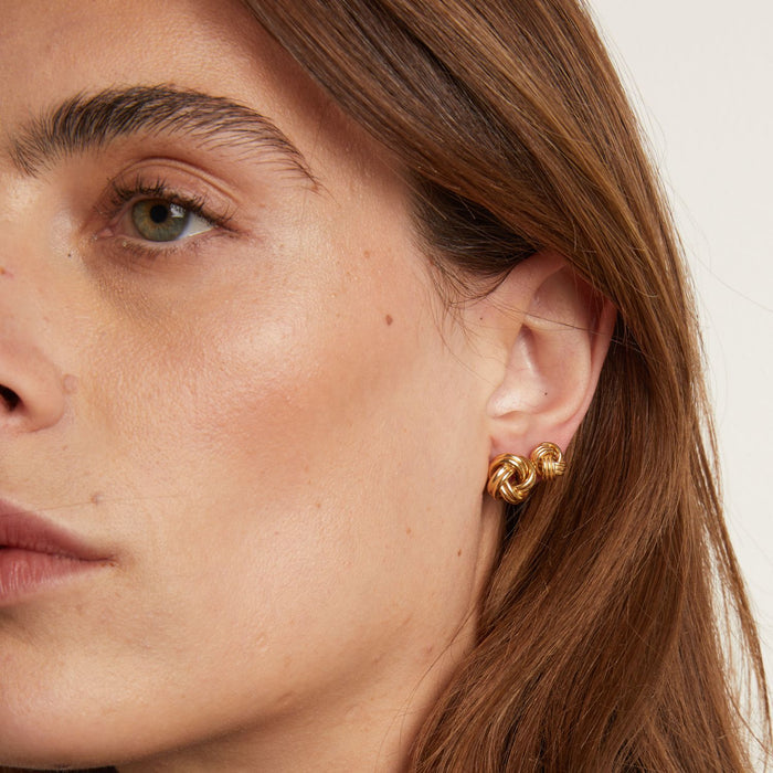 Model. Close-up of a person wearing gold hoop earrings with a neutral background