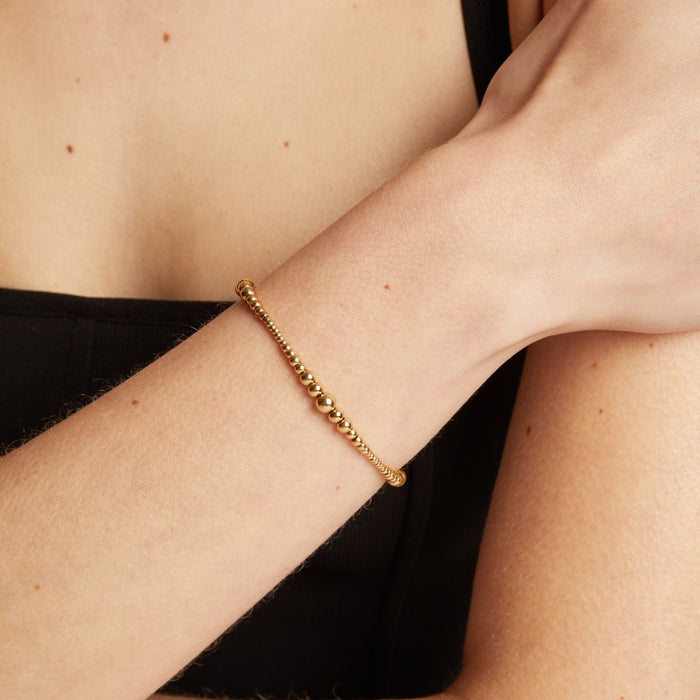 Model. Gold bracelet on a person's wrist with a neutral background.
