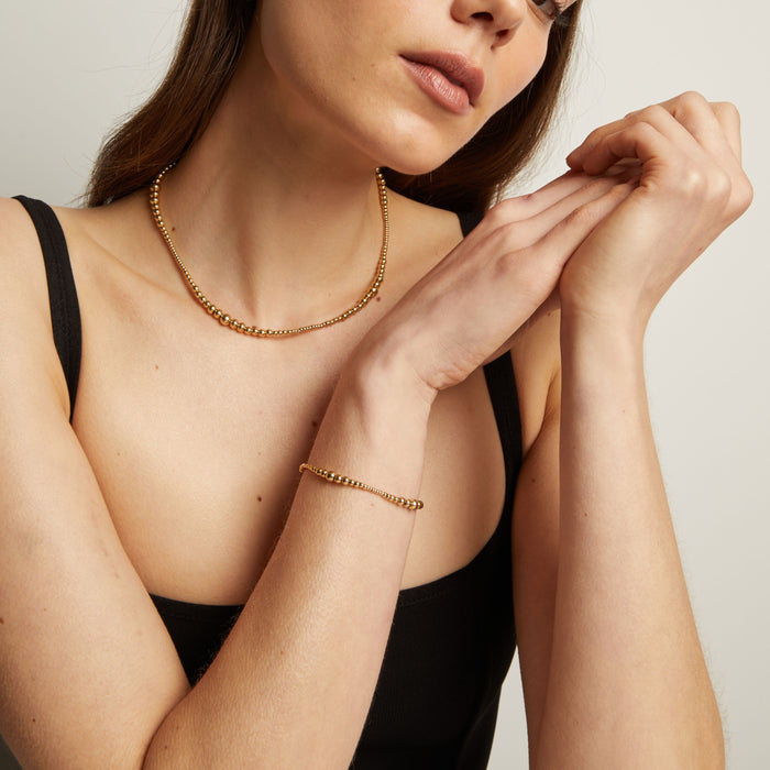 Model. Woman wearing gold necklace and bracelet against a neutral background.