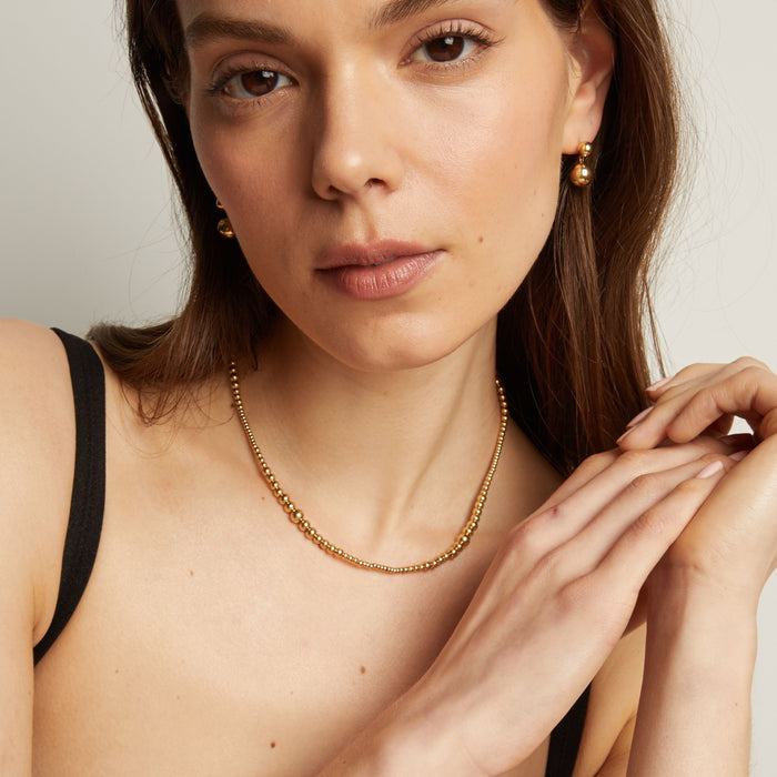 Model. Woman wearing a gold necklace with a neutral background.