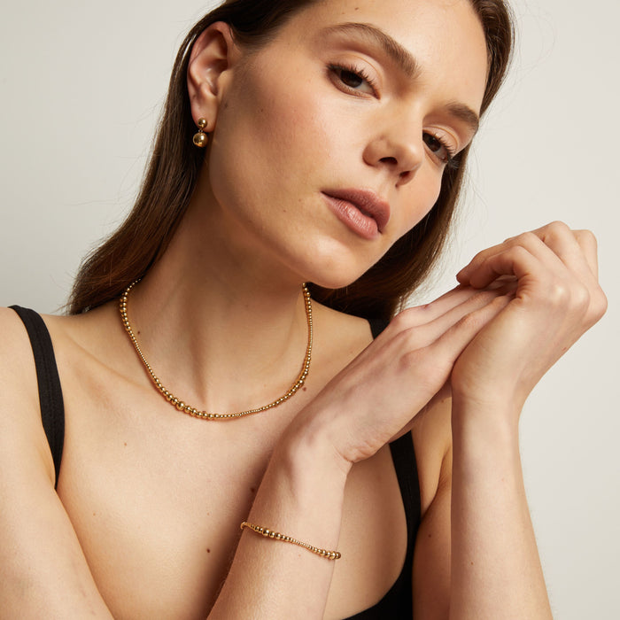Model. Woman wearing a gold necklace and bracelet with a neutral background.