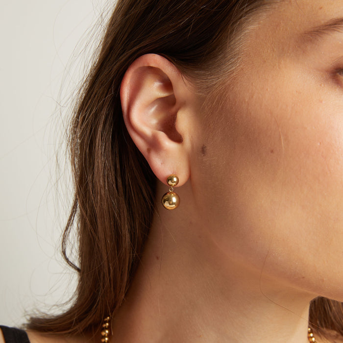 Model. Close up of a person wearing gold earrings with a plain background.