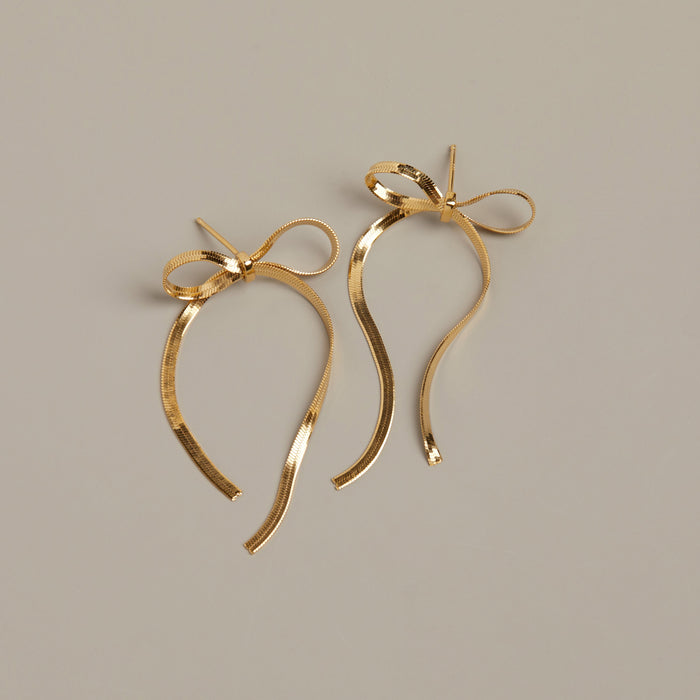 Flatlay Model. Gold bow earring on beige background