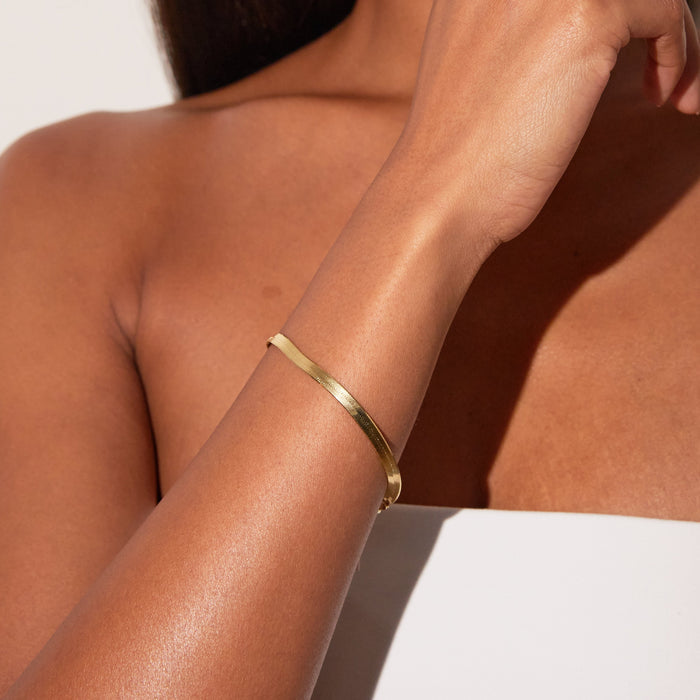 Model. Gold bracelet on a person's wrist with a neutral background