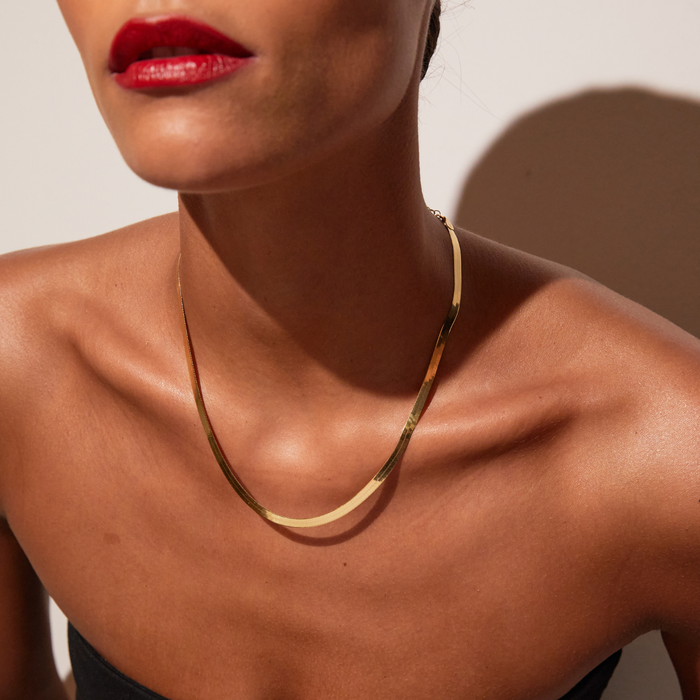 Model. Close-up of a person wearing a gold necklace with a neutral background