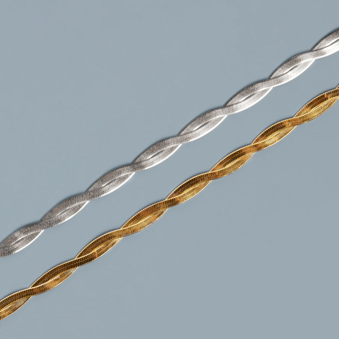Model. Two braided hair sticks, one silver and one gold, on a gray background.