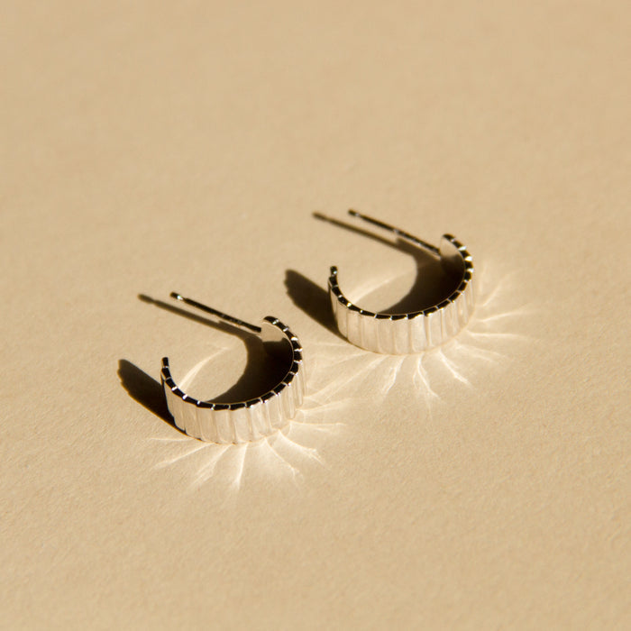 Lifestyle Model. A close-up flatlay shot of two gold hoop earrings.