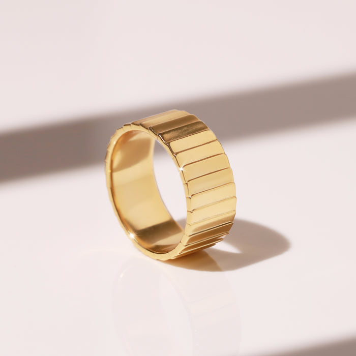 Model. A close-up flatlay shot of a thick gold band ring on white background.