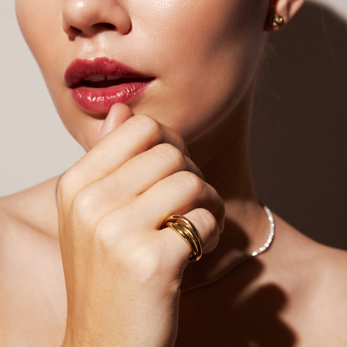 Model. A close-up of a woman's hand wearing a delicate gold ring with three intertwined bands.