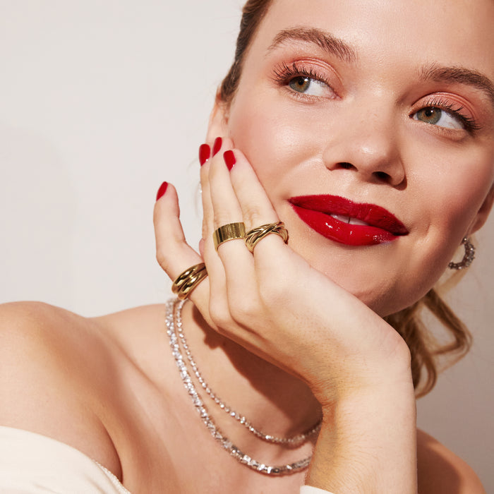 Model. A woman wearing a 3 gold rings and 2 tennis necklaces on neutral background.