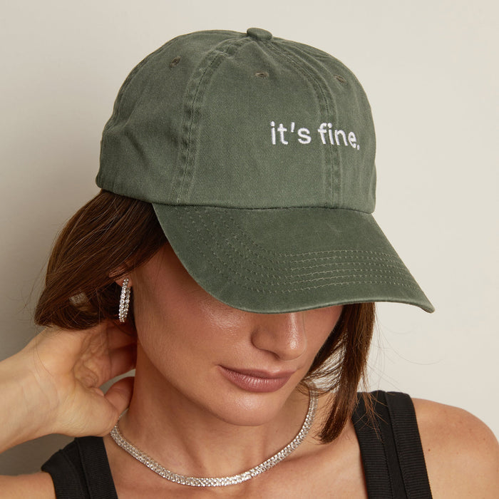 Model. Person wearing a green cap with 'it's fine' text on a neutral background