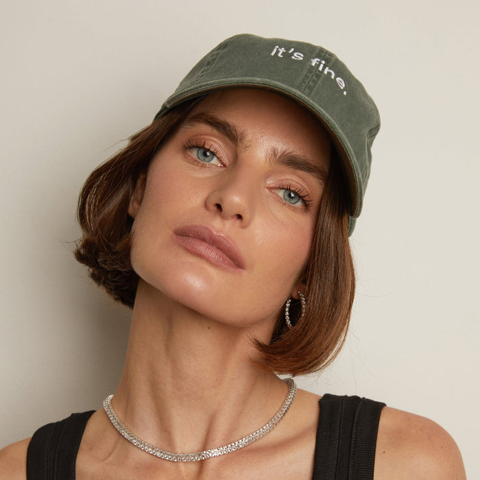 Model. Person wearing a green cap with 'it's fine' text on a neutral background