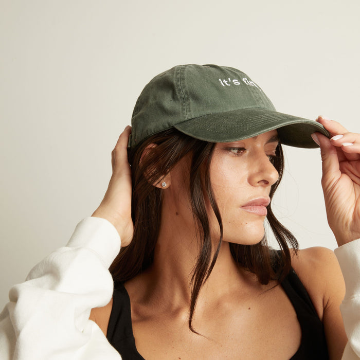 Model. Woman wearing a green cap with 'it's fine' text on a plain background