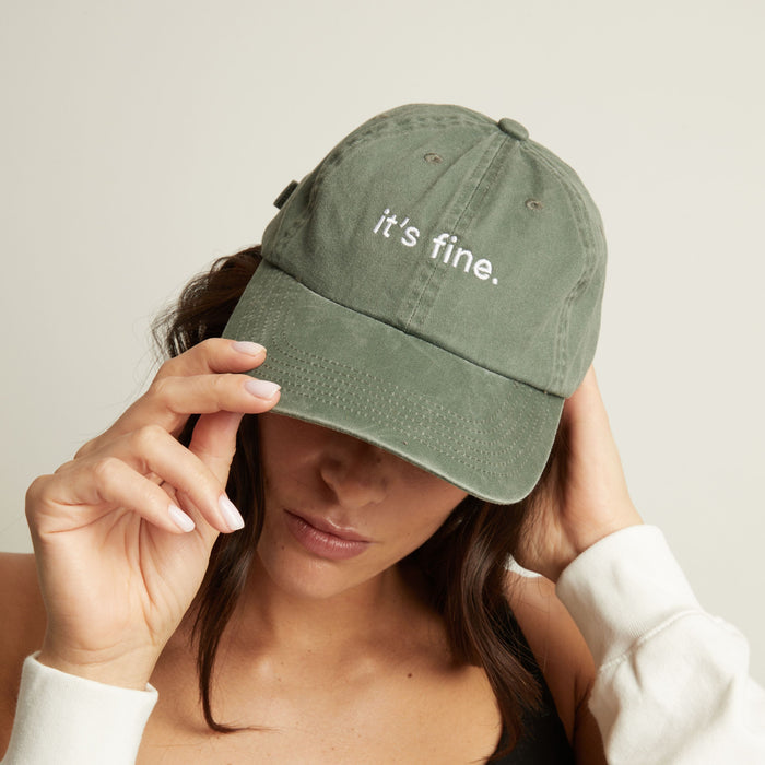 Model. Woman wearing a green cap with 'it's fine' text on a plain background