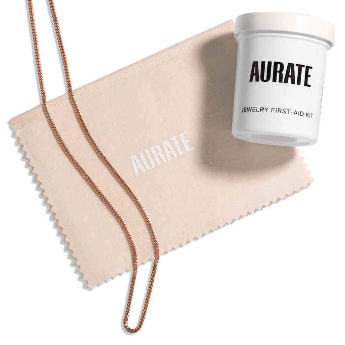 Model A closed jar of the Aurate Jewelry First-Aid Kit resting on a branded polishing cloth next to a gold chain necklace.