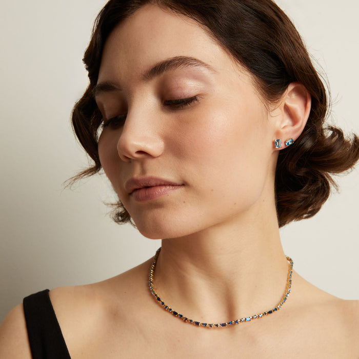 Close-up of a woman wearing a blue necklace and earrings against a neutral background. Model