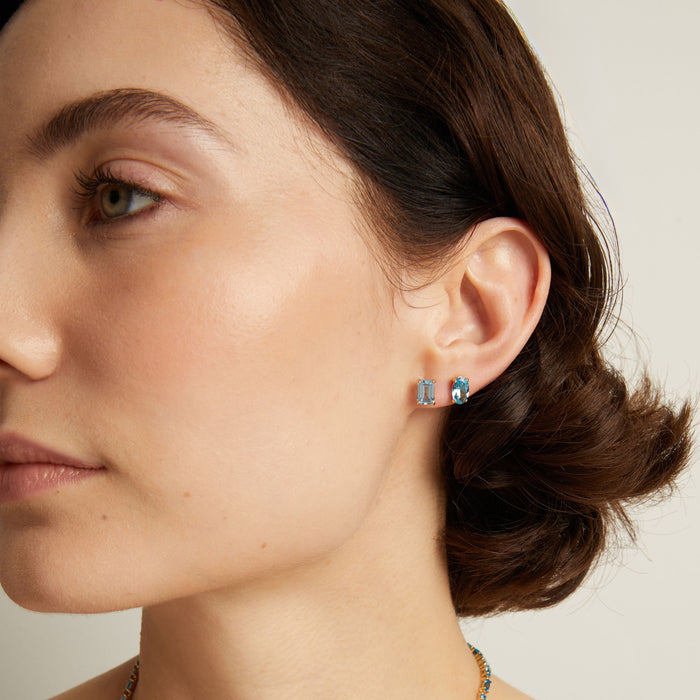 Woman wearing two blue stud earrings.