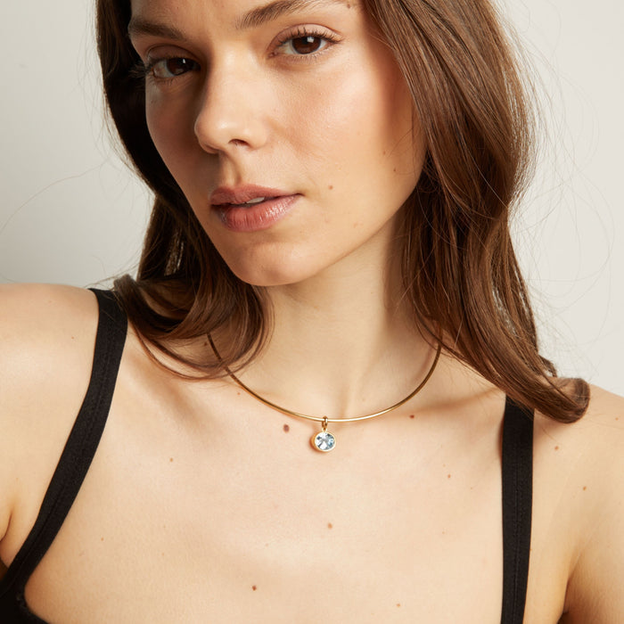Model. Close up of a woman wearing a gold necklace with an aquamarine pendant.