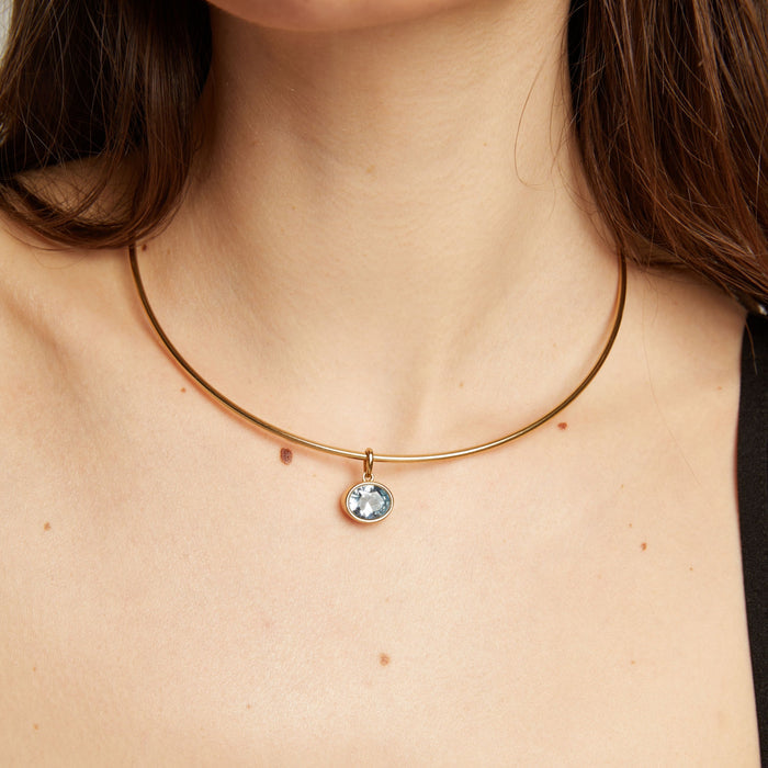 Gold necklace with an aquamarine pendant worn by a woman.