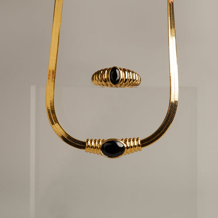 Model. Gold necklace with black beads on a gray background