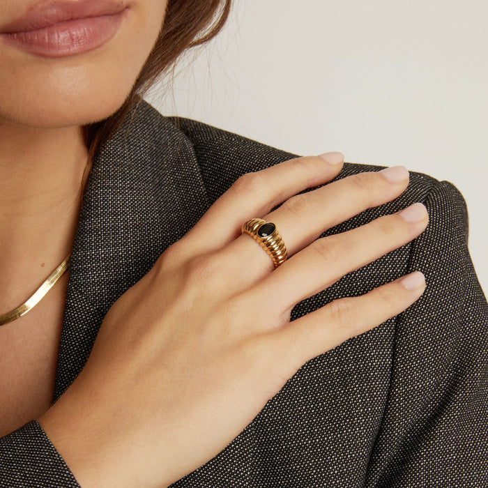 Model. Close-up of a hand wearing a gold ring with a black stone, holding a textured gray fabric.
