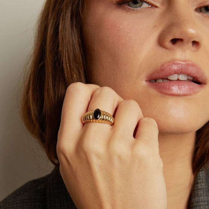 Model. Close-up of a woman wearing a gold ring with a black gemstone.