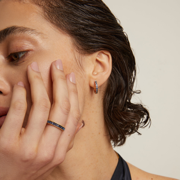 Model. Close-up of a woman wearing a blue gemstone earring and ring on a neutral background