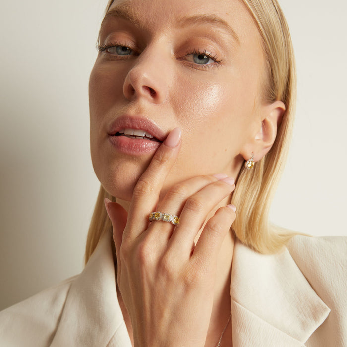 Model. Woman wearing a gold ring and earrings against a neutral background