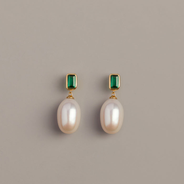 Model. Pair of pearl earrings with emerald green gemstones on a beige background