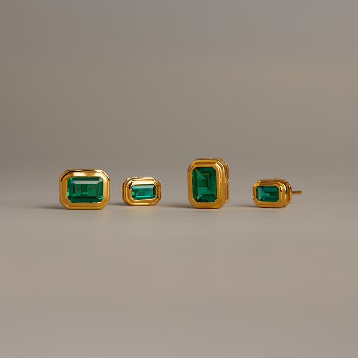 Model. Set of gold earrings with green gemstones on a beige background