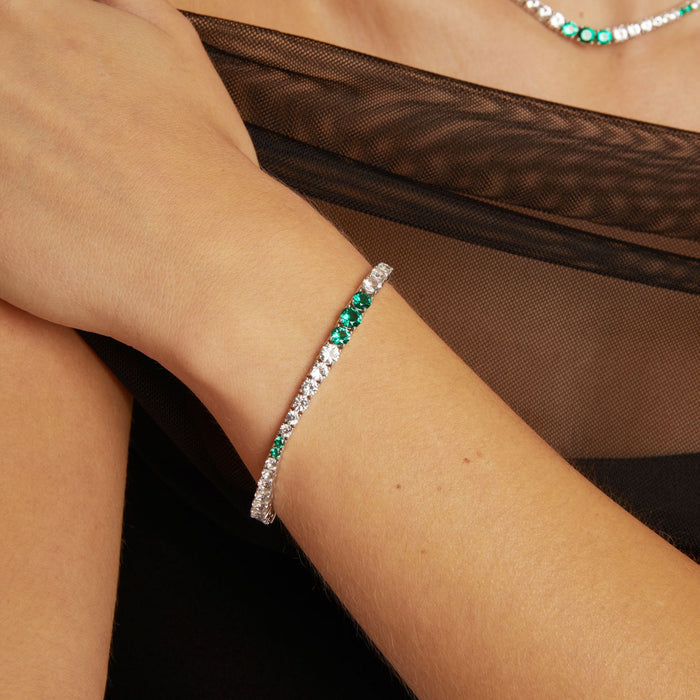 Model. Close-up of a wrist wearing a bracelet with green and clear stones, against a brown fabric background.