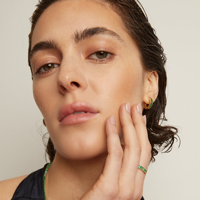 Model.  Woman wearing green hoop earring in front of neutral background