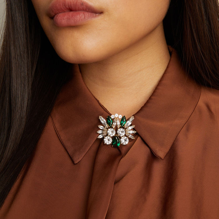 Model. Close-up of a woman wearing a brown shirt with a decorative brooch on the collar.