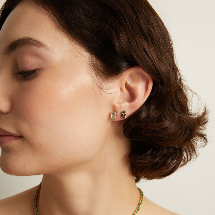Close-up of a person wearing green gemstone stud earrings with a neutral background. Model