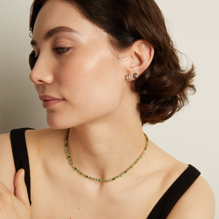 Woman wearing a green tennis necklace and earrings on a neutral background. Model