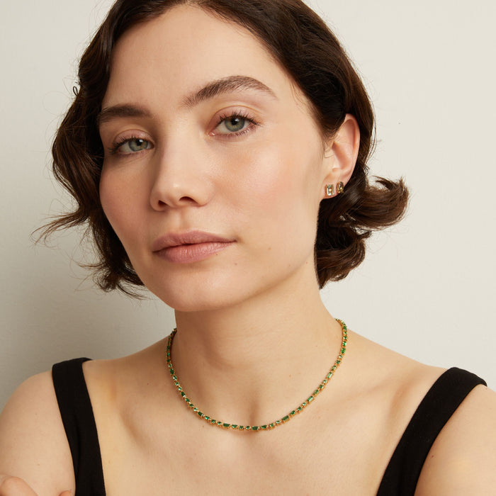 Woman wearing a green tennis necklace and earrings on a neutral background. Model