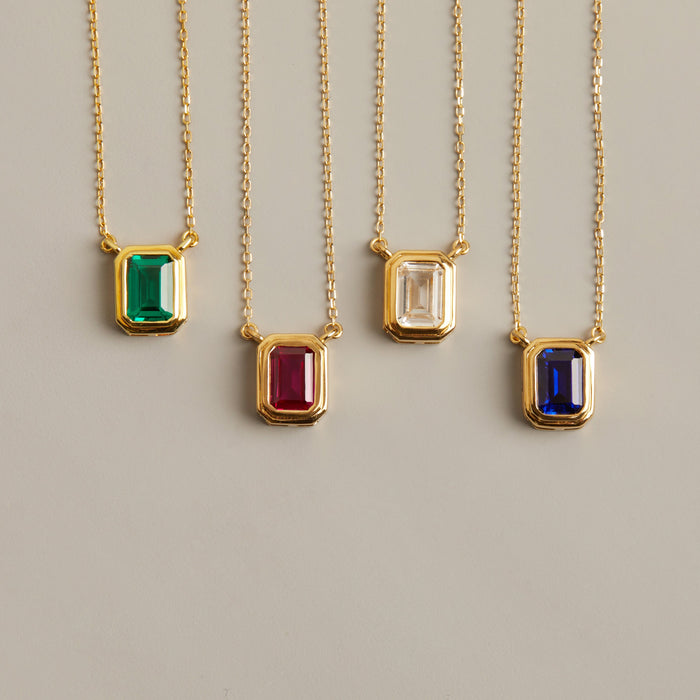Model. Four gold necklaces with gemstone pendants on a light gray background