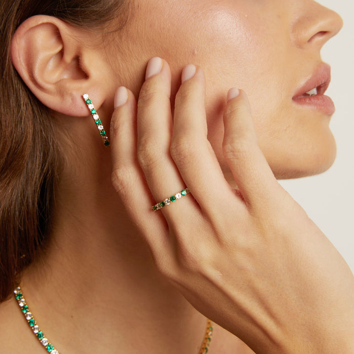 Model. Close-up of a woman wearing emerald green hoop earrings and a ring, with a neutral background.