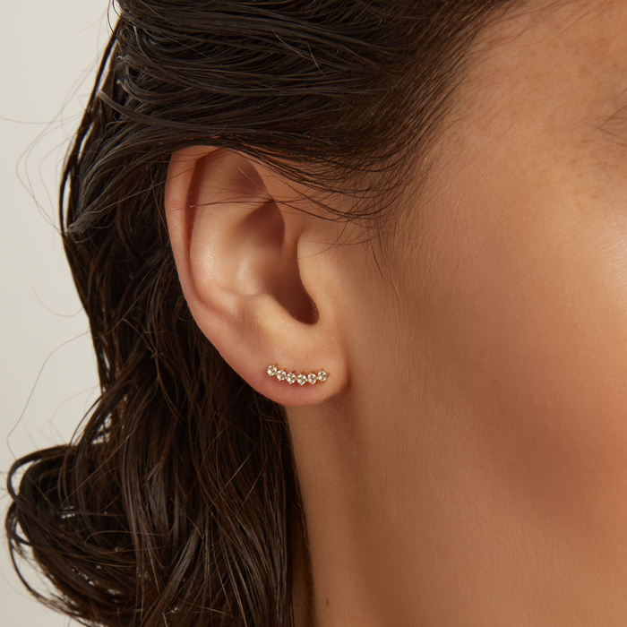 Close-up of an ear wearing a small earring with a neutral background.